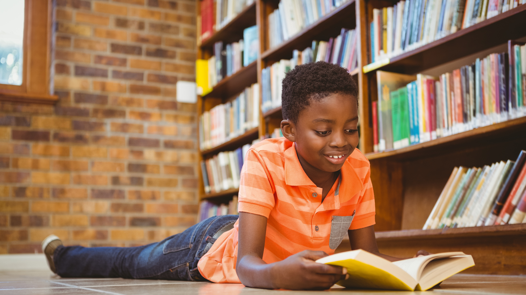 A boy reading on the floor of a library.