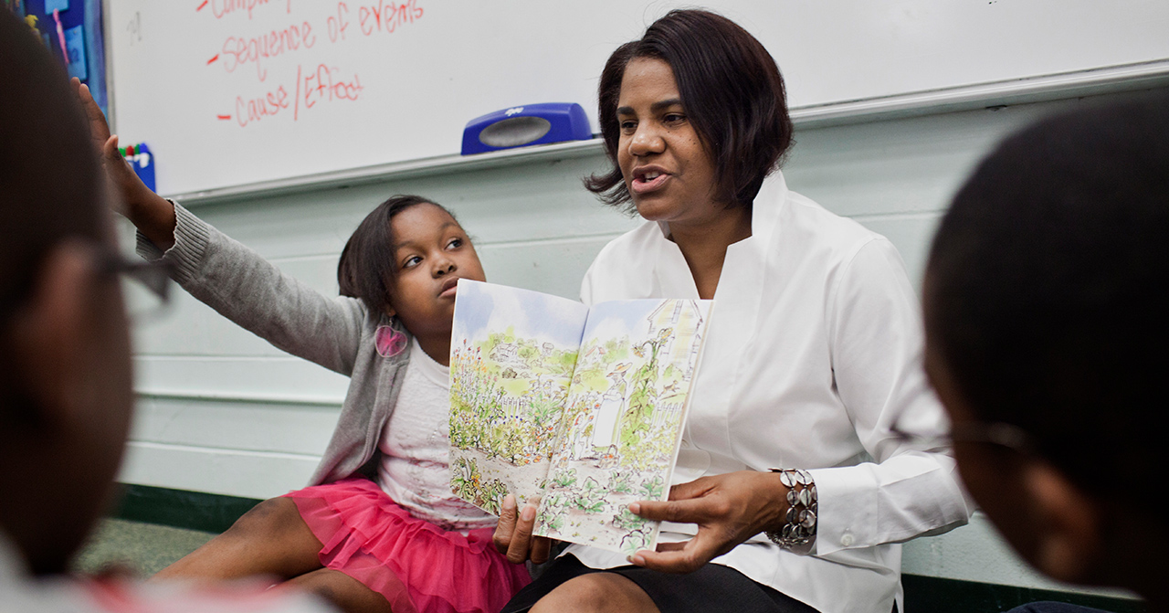 A woman reading to children on the floor and one child has their hand raised. 