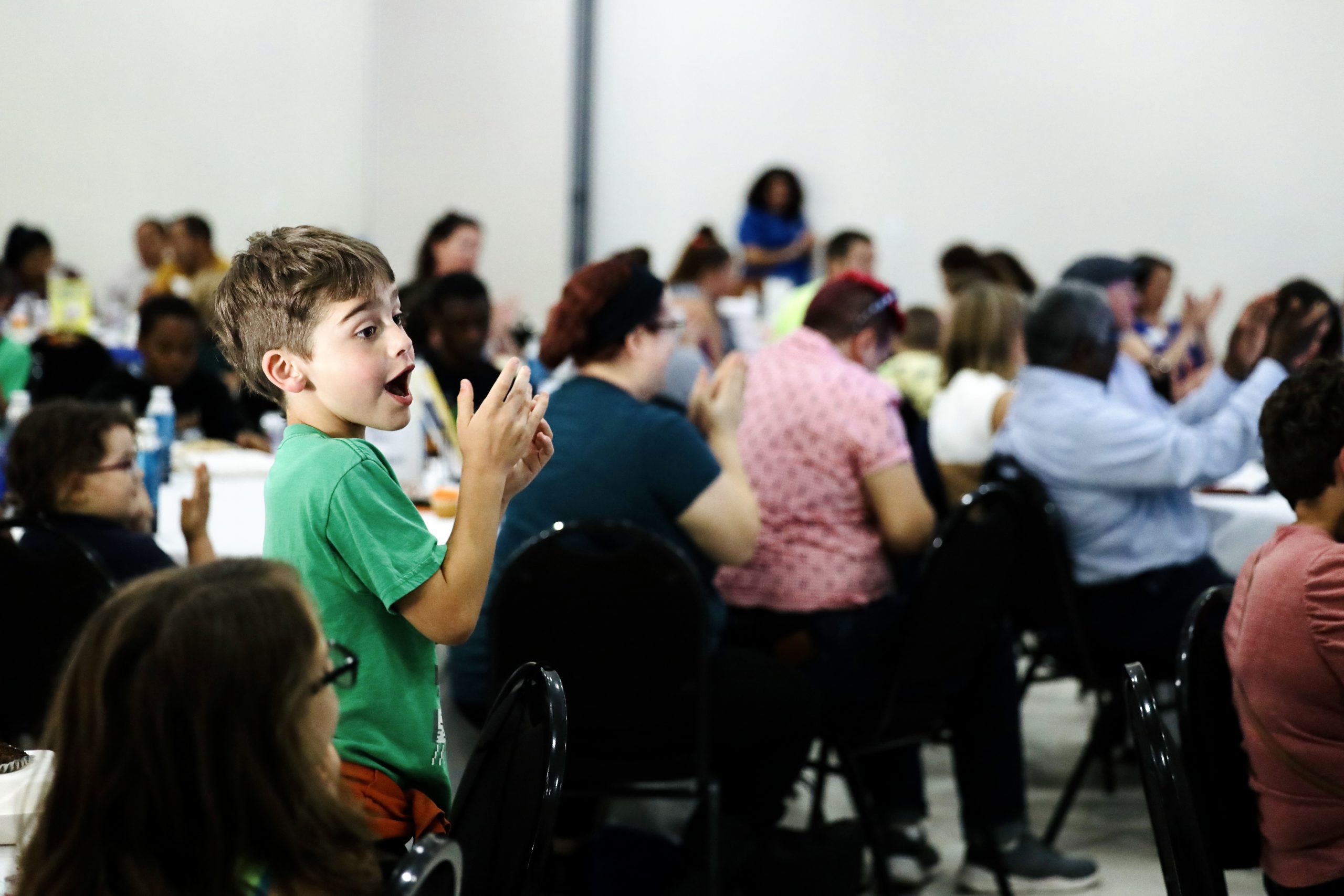 A child standing and clapping in a room of people. 