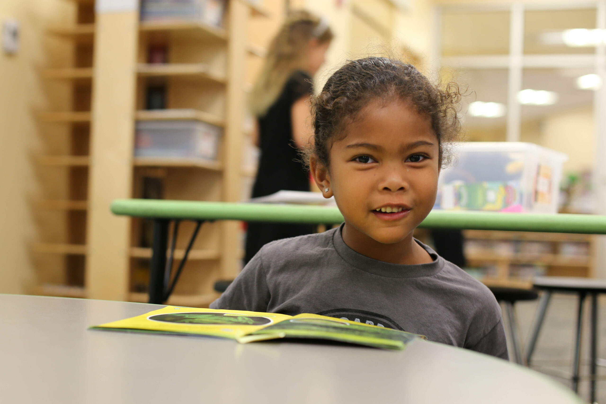 A child smiling at the camera with a book in front of them 