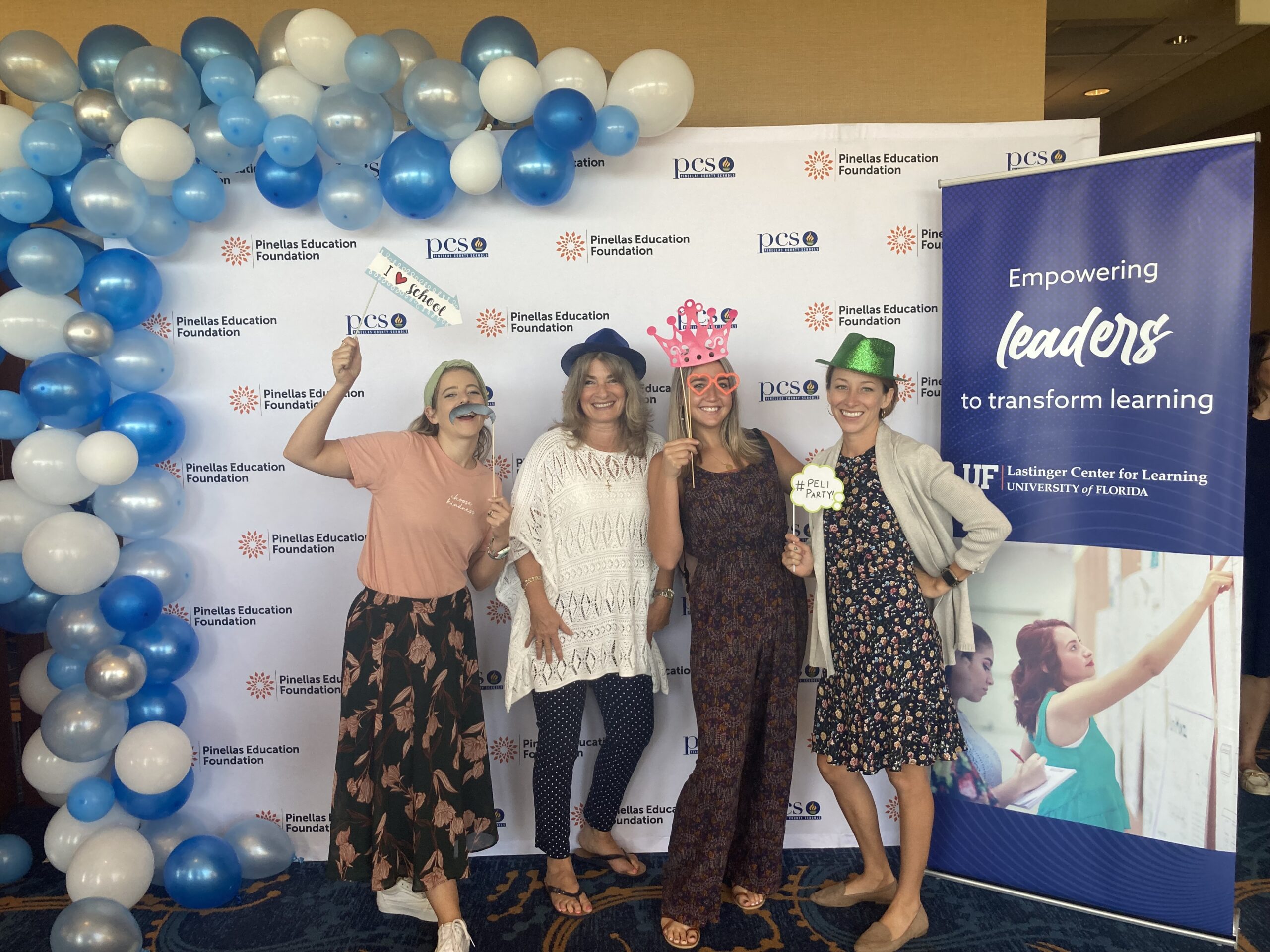 4 teachers use props at the photo-booth - a mustache, a blue sparkly hat, a pink hat, and a green sparkly hat