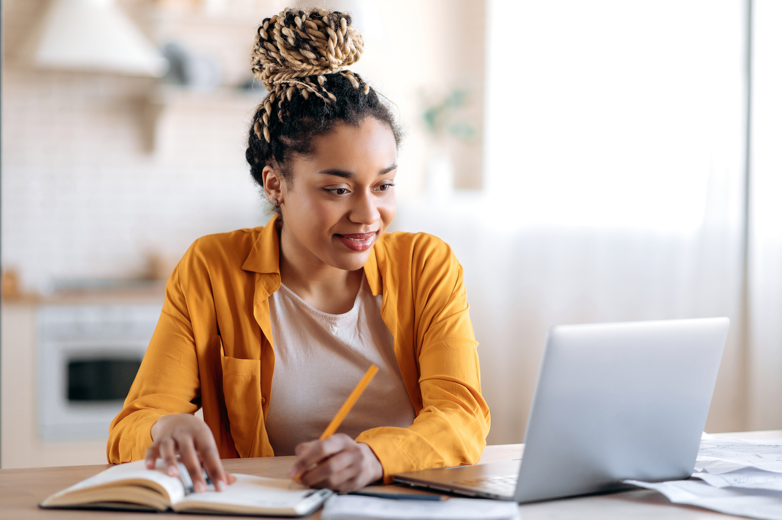 A young woman takes notes while sitting at her laptop.