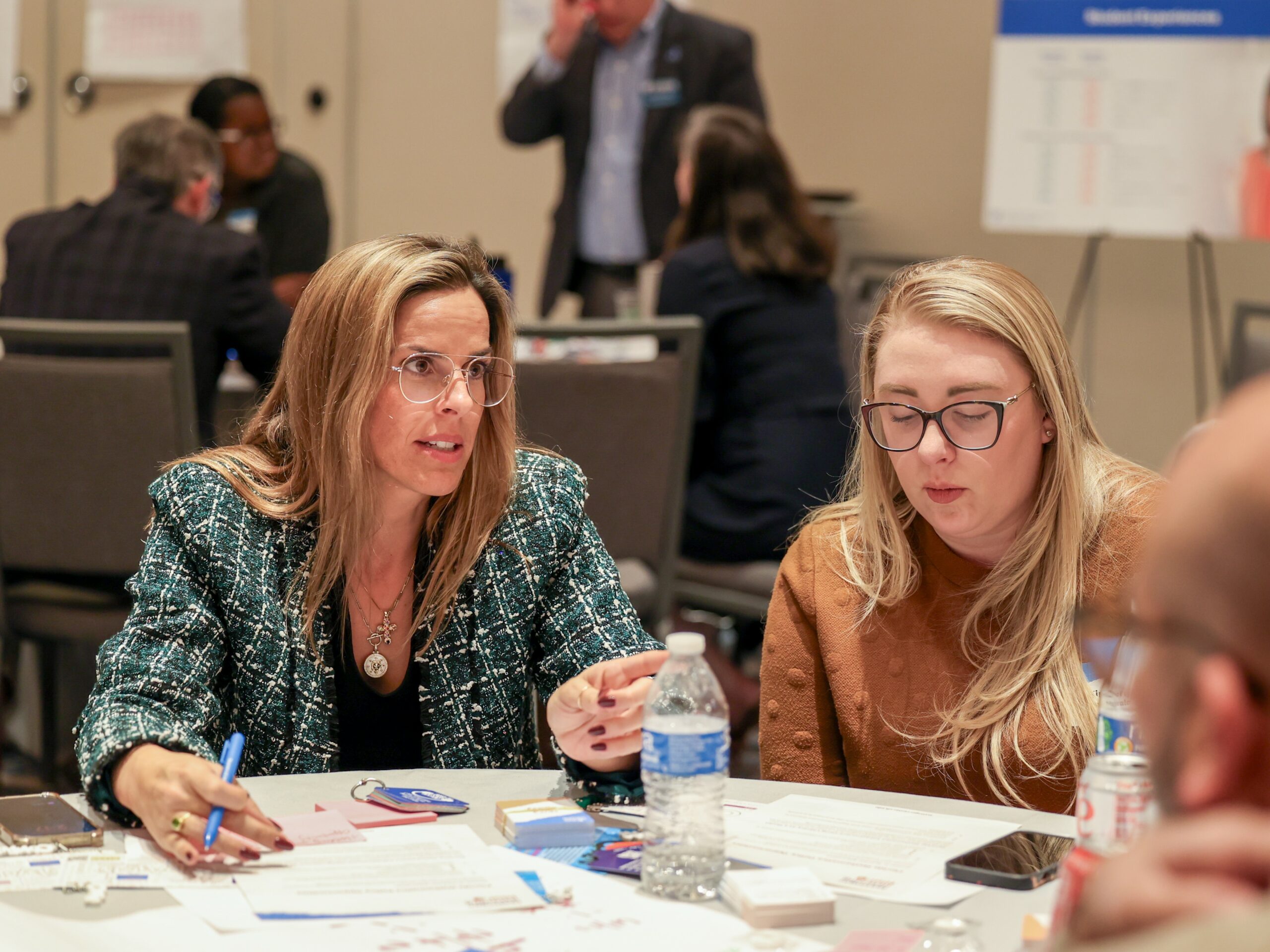 Two women (Math Summit attendees) sit at a round table discussing the current agenda item of the summit.