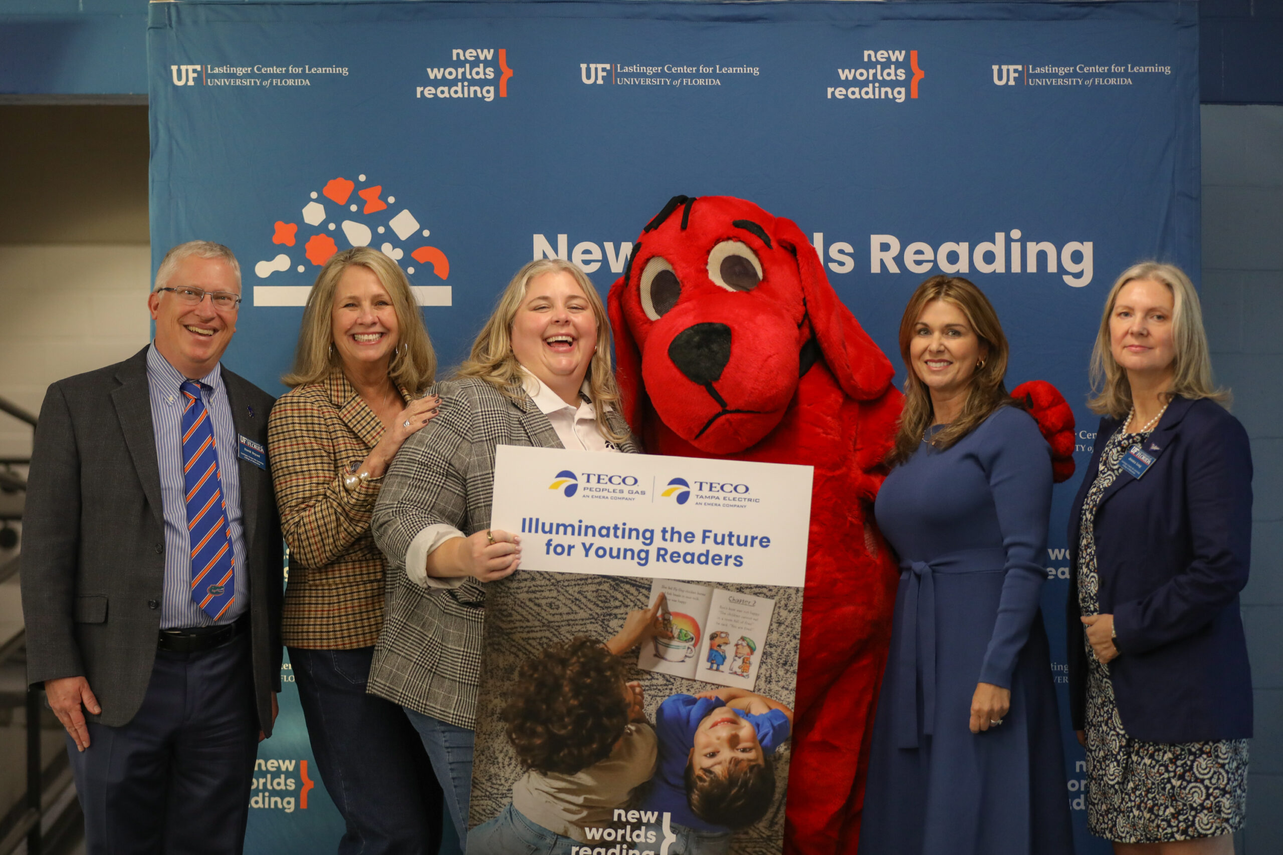 Several donors from TECO and staff of New Worlds Reading standing with a costumed Clifford the Big Red Dog, holding a sign sponsored by TECO that says "Illuminating the Future for Young Readers."