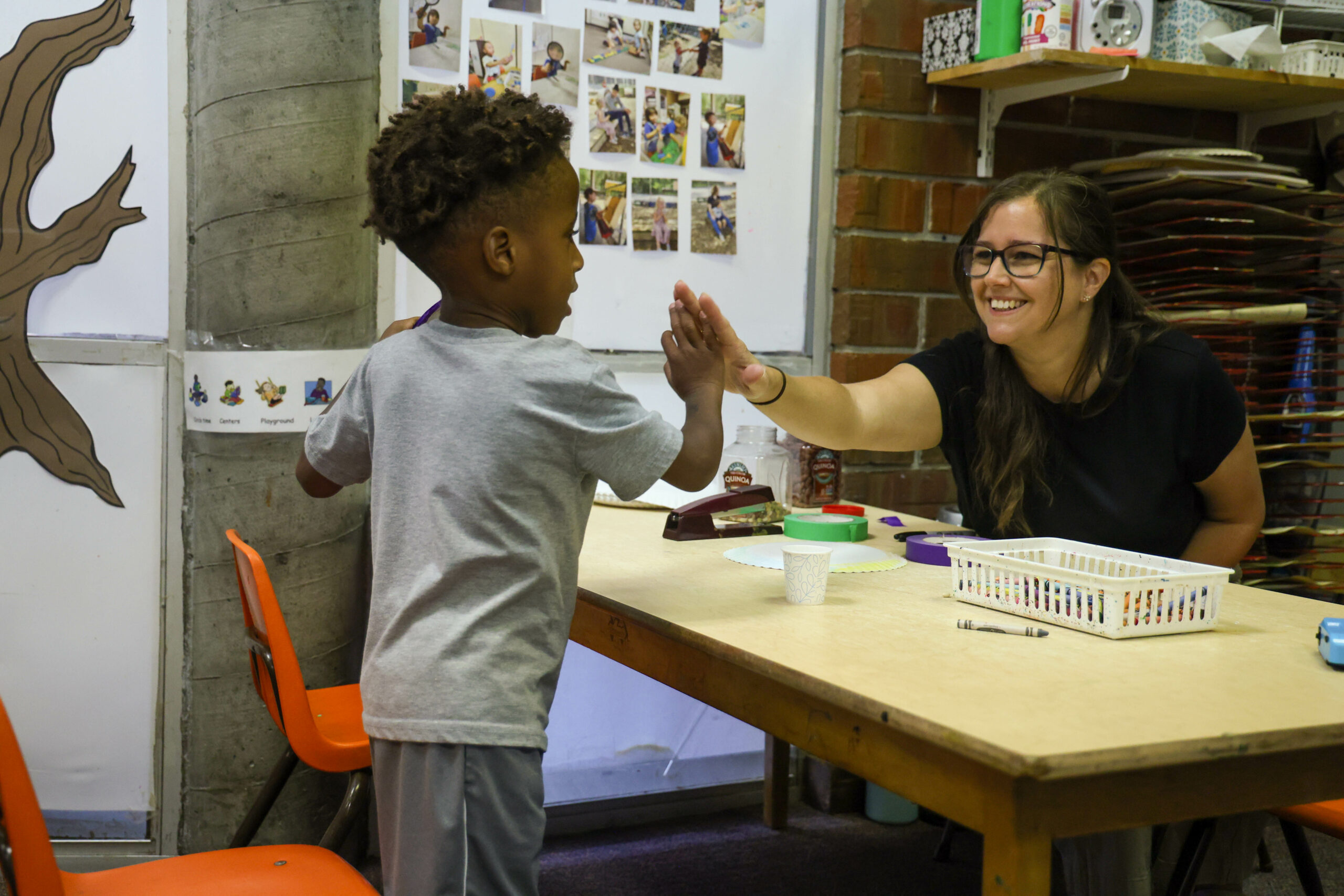 An early learning educator high-fiving a young student in their classroom.